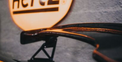 Close-up of a car spoiler with a glowing Hertz sign in the background.
