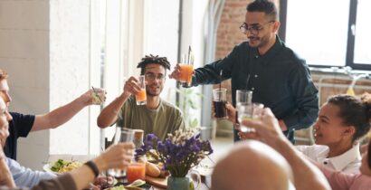 Group of friends toasting drinks during a lively indoor meal, enjoying togetherness and celebration.