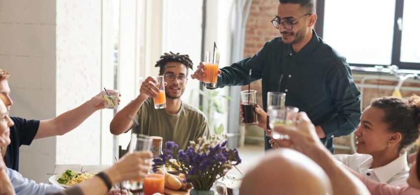 Group of friends toasting drinks during a lively indoor meal, enjoying togetherness and celebration.