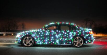 Car covered in bright Christmas lights parked outdoors at night. Festive holiday theme.
