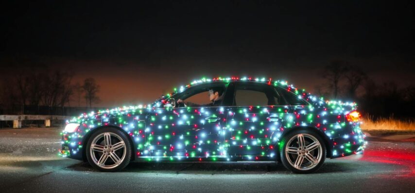 Car covered in bright Christmas lights parked outdoors at night. Festive holiday theme.