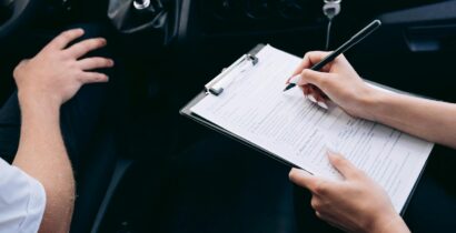 Close-up of a person writing on a clipboard inside a car, showing hands and a gear shift.