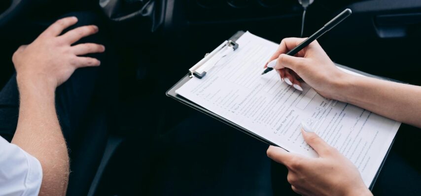 Close-up of a person writing on a clipboard inside a car, showing hands and a gear shift.